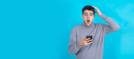 surprised young man with mobile phone or smartphone isolated on blue background