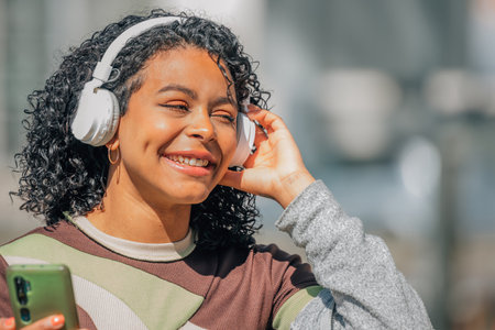 latin girl with afro hair with headphones and mobile phone in the streetの写真素材