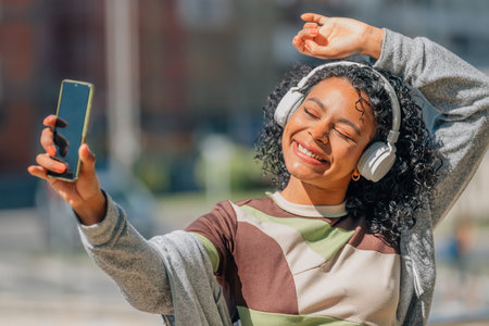 latin girl with afro hair with headphones and mobile phone in the streetの写真素材