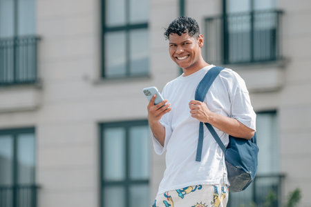 young man or latin student with mobile phone on the street with backpackの写真素材
