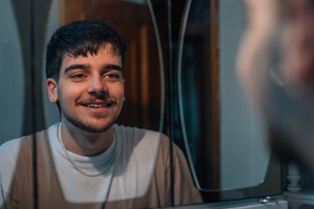 young man smiling looking at himself in the mirror at homeの写真素材
