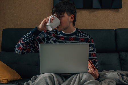 young man at home drinking coffee looking at computerの写真素材