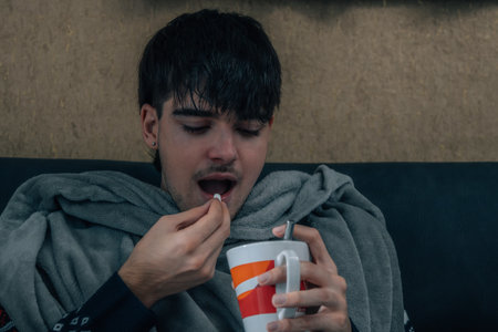 sick young man with a cold holding a cup of hot tea or coffeeの写真素材
