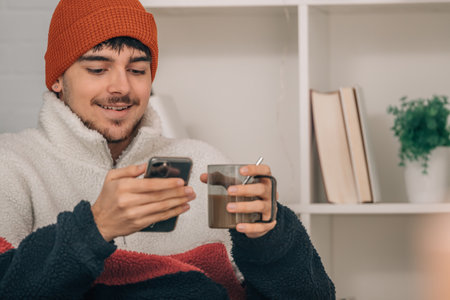 young man at home warm with cup of coffee and mobile phoneの写真素材