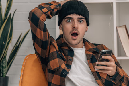 young man at home with mobile phone and surprised expression