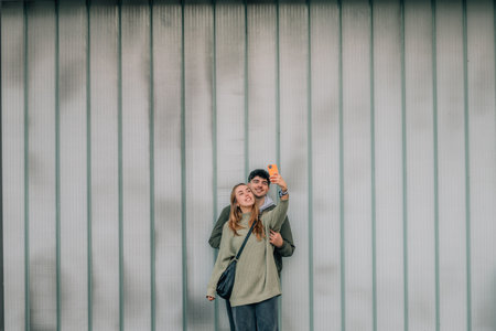 urban young couple with mobile phones on the street wall taking a selfieの写真素材