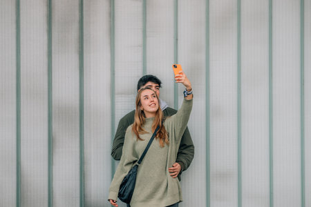 urban young couple with mobile phones on the street wall taking a selfie