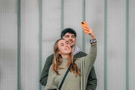 urban young couple with mobile phones on the street wall taking a selfieの写真素材