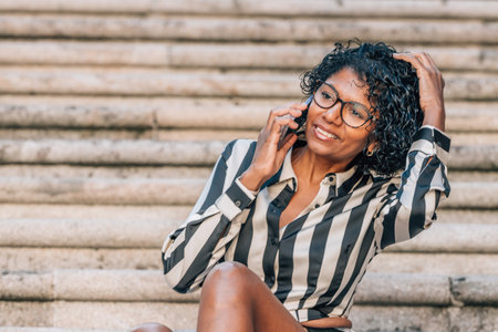 latin african american woman sitting on the street with mobile phoneの写真素材