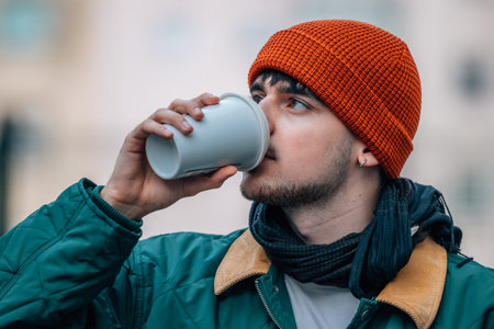 young man on the street drinking with cup in winterの写真素材
