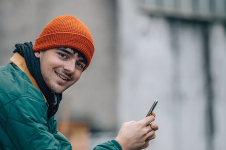 portrait of young man with hat and warm clothes looking at mobile phoneの写真素材