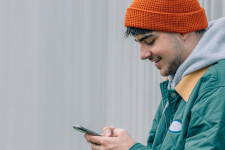 young man with mobile phone on outdoor wall background wearing winter clothesの写真素材