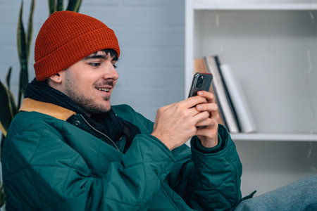 young man at home with mobile phone wearing warm or winter clothes