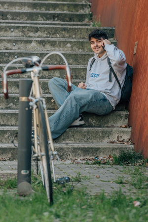 student sitting on the street with mobile phone and bicycleの写真素材