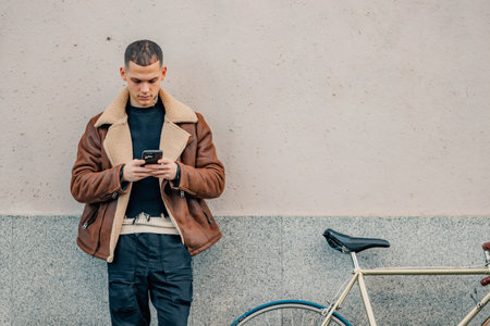 fashionable young man with mobile phone and bicycle in urban background