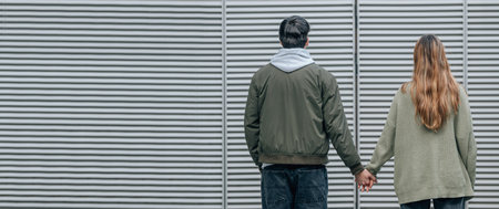 young couple on the street with their backs to each other holding handsの写真素材