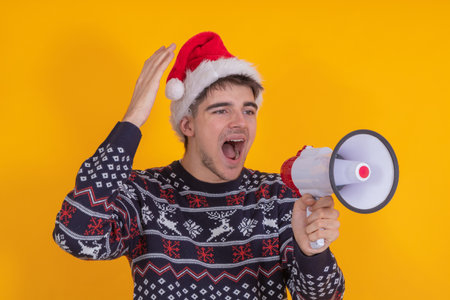 young man with santa claus hat isolated shouting with loudspeakerの写真素材