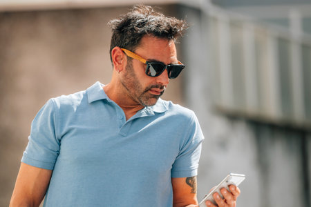 attractive young man with sunglasses looking at his mobile phone on the street outdoorsの写真素材