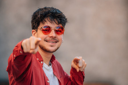 Young man with smiling sunglasses pointing with his hands to cameraの写真素材