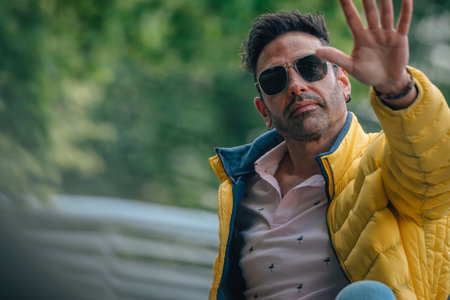 hispanic man with urban style sunglasses on the street wavingの写真素材