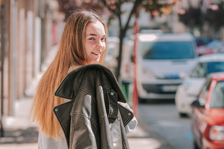 young blonde long-haired girl walking on the street with jacket behind her back