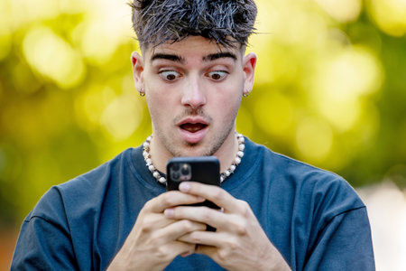young man or teenager on the street with mobile phone and surprised expression