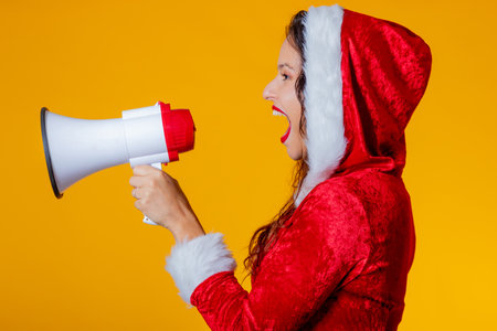 young woman wearing santa claus costume isolated shouting with megaphoneの写真素材