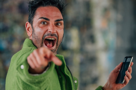 young man on the street with mobile phone shouting and pointingの写真素材