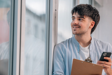 young man with mobile phone and documents next to the window