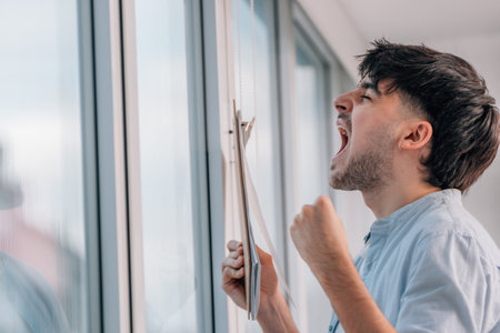 young man with folder screaming from euphoria indoorsの写真素材
