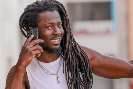 young man with afro hair or dreadlocks talking on mobile phone on the street