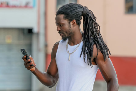 young man with afro hair or dreadlocks looking at his mobile phone on the street