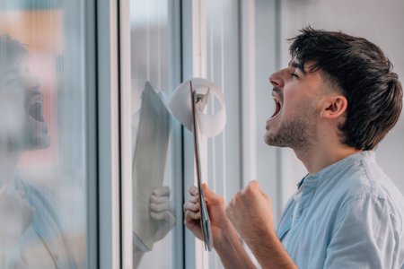young man with folder screaming from euphoria indoorsの写真素材