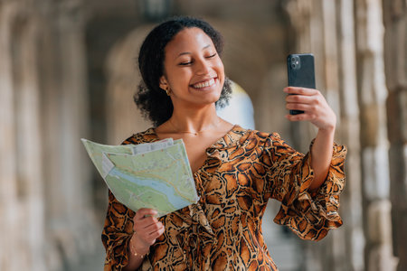 smiling latina woman traveling with map and phone on the streetの写真素材