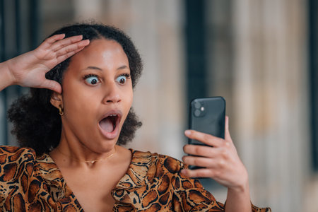 portrait of a young hispanic latina woman with a phone and a surprised expressionの写真素材