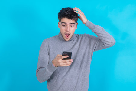 surprised young man with mobile phone or smartphone isolated on blue backgroundの写真素材