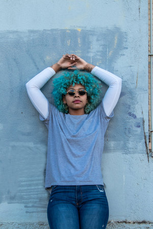 young woman in sunglasses with blue hair relaxing on street wallの写真素材