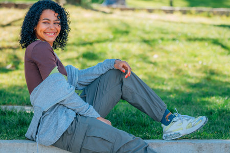 smiling brunette hispanic young girl or woman with afro hair smiling sitting on the streetの写真素材