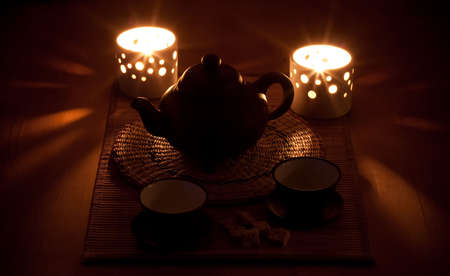 Tea drinking. The clay Chinese teapot, two candles, two cups and sugar on a wooden table.の写真素材