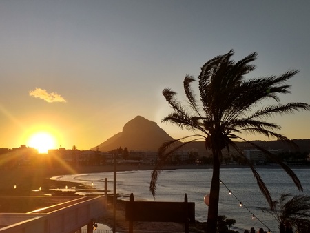 Sunset over the sea bay towards a mountain at Xavier in Spain near Alicante in Summer with colourful skies and palm tree moving in the evening breeze of theの写真素材