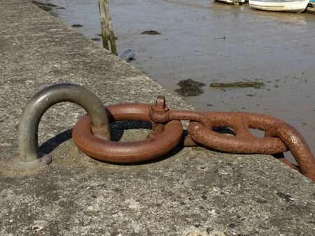 Close up macro of old metal chain links with bolts on iron and steel anchor in concrete stone wall at harbour where boats mooring with sea water outdoor landscapeの写真素材