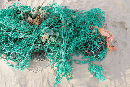 Close up of beautiful fisherman fishing nets string on sandy beach, bird's eye view of the blue green brown string cotton nylon net against the white beautiful sand with pebbles shells on Autumn dayの写真素材
