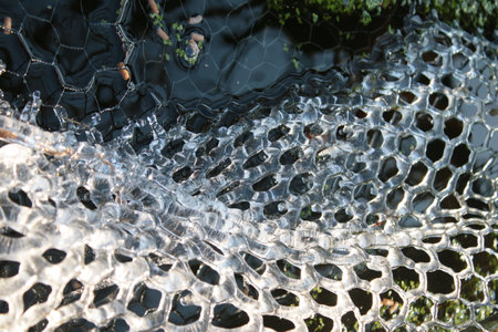 Close up of frozen water in freezing Winter weather white transparent pattern of hexagons on metal wire covering garden natural pond frost drips as melts as weather brightens on freezing cold dayの写真素材