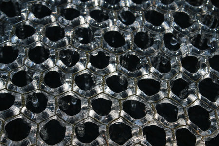 Close up of frozen water in freezing Winter weather white transparent pattern of hexagons on metal wire covering garden natural pond water drips as melts as weather brightens on freezing cold dayの写真素材