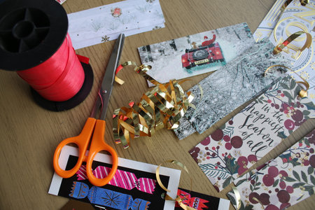 Close up of recycled hand made craft Christmas gift tags made previous year family friend cards the designs cut into oblong and square shapes tied gold metallic string, scissors and red string reelの写真素材