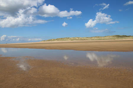 Landscape of beautiful sandy beach with no people and sands stretched to horizon with white puffy clouds reflected in the water pools in Holkham north Norfolk East Anglia ukの写真素材