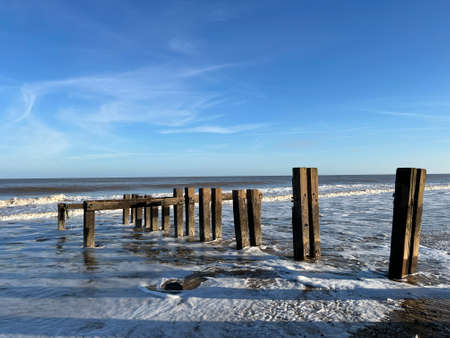 Landscape of ocean from sandy beach he beautiful calm sea gentle waves and blue skies looking to horizon with wood defence structure from shore on bright cold Winter day Norfolk ukの写真素材