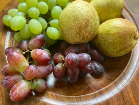 Close up of fruit on hand made turned wood platter with pears and green and red grapes the ripe delicious raw fruits ready for vegetarian salad desert dish flat lay view with naturの写真素材