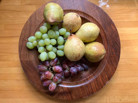 Close up of fruit on hand made turned wood platter with pears and green and red grapes the ripe delicious raw fruits ready for vegetarian salad desert dish flat lay view with naturの写真素材