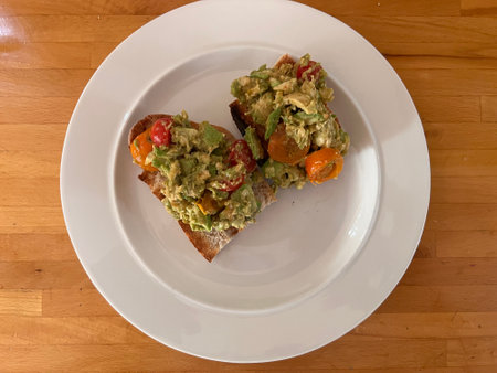 Avocado and tomato sandwich on a white plate on a wooden table